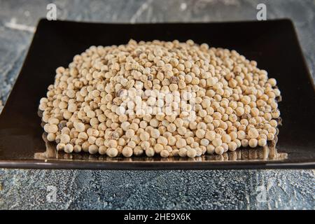 White peppercorns on black plate with reflection Stock Photo