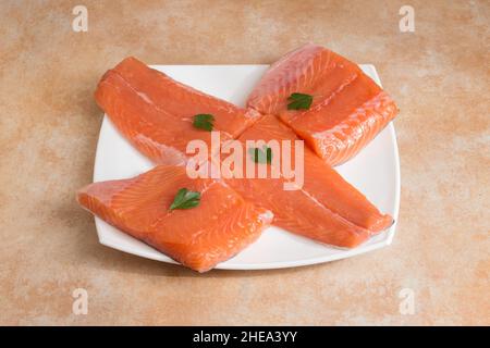 Half fresh salmon just cut into loins garnished with fresh parsley leaves on an elegant white tray on a pastel-colored textured marble table. Stock Photo