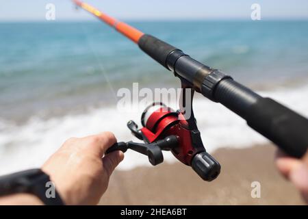 Hands hold a fishing rod against the background of sea coast Stock Photo