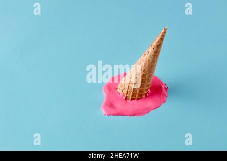 Dropped upside down ice cream cone with melting scoop on pastel blue floor. Minimalistic summer food concept. Stock Photo