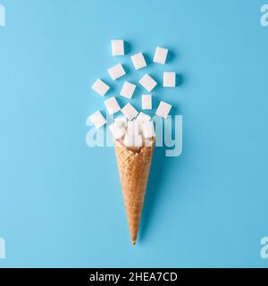 Sugar cubes on ice cream cone on blue background. Minimalistic sweet food addiction and sugar diet for health concept. Stock Photo