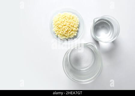 Candelilla Wax in Chemical Watch Glass and alcohol in beaker place on white laboratory table. Top view Stock Photo