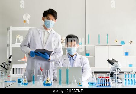 Two scientists with face mask and gown working in laboratory. Omicron strain testing process, Coronavirus disease 2019. Stock Photo