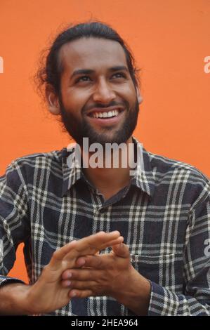 Selective focus of a bearded young man smiling while looking sideways, posing against orange wall background Stock Photo