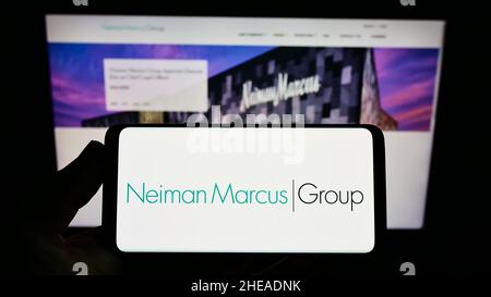 Person holding smartphone with logo of US retail company Neiman Marcus Group Inc. on screen in front of website. Focus on phone display. Stock Photo