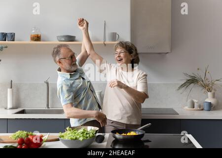 Happy middle aged man dancing with laughing elderly senior wife. Stock Photo