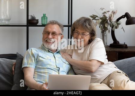Happy bonding dreamy older couple using laptop. Stock Photo