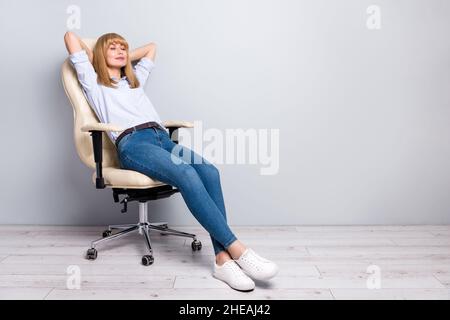 Photo of cute woman wear shirt having rest cozy armchair arms behind head empty space isolated grey color background Stock Photo