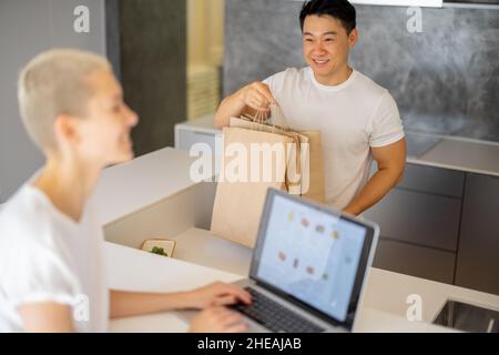 Woman choosing groceries online and man with bags Stock Photo