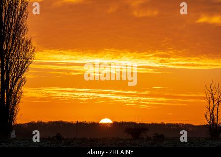 Winter dawn sky  with the sun just rising above a on a low horizon against a orange sky with a band of underlit clouds, cumulus mediocris, at Broomfield in Kent, England. Stock Photo