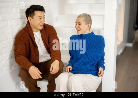 Asian man hugging caucasian wife on stairs at home Stock Photo