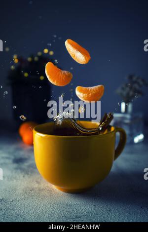 Tea splash composition on a dark blue background. Slices of mandarins are placed in splashes. Splashes of tea fly out of a cup Stock Photo