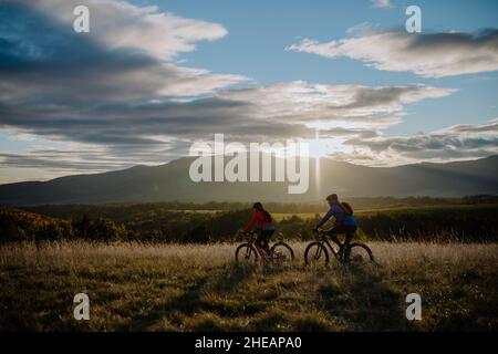 Active senior couple riding bikes outdoors in autumn nature at dusk. Stock Photo