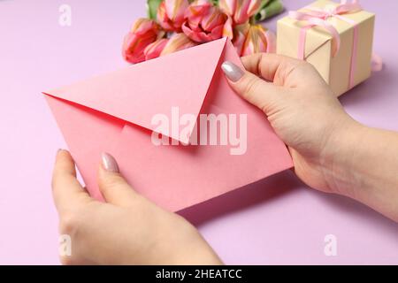 Female hands hold envelope on violet background with flowers and gift box Stock Photo