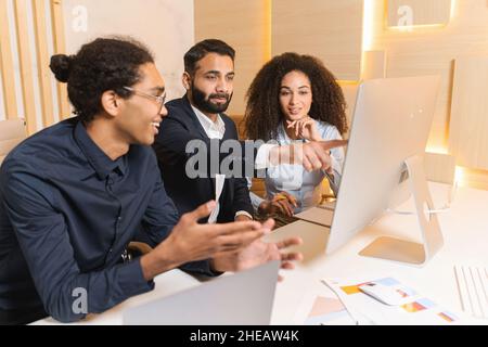 Discussion of successful multiracial team during a morning meeting at the office. Brunette guy pointing at the computer screen. Brainstorming concept Stock Photo