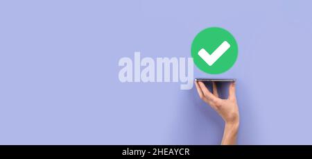 Hand holds green icon Check mark,Check Mark Sign, Tick Icon,right sign,circle green checkmark button,Done.On grey background.Banner.Copy space.Place f Stock Photo