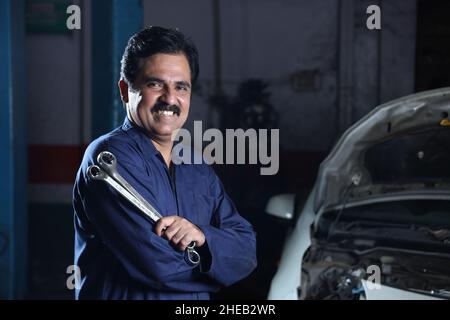 Portrait of a happy Indian car mechanic smiling and holding car repairing tools in hand while he is in working a workshop Stock Photo