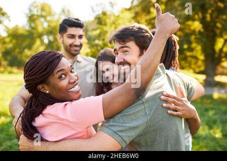 Young woman with thumbs up celebrating success together with team colleagues in the park Stock Photo