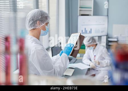 Young scientist in lab coat typing on digital tablet and working online while standing in the lab Stock Photo