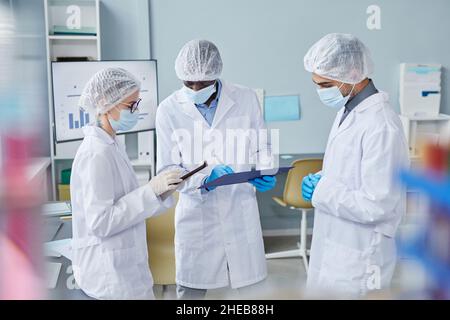 Group of scientist in lab coats using tablet pc and making notes in medical card while doing research in hospital laboratory Stock Photo