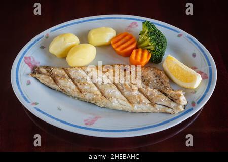 Grilled sea bass file with baked potatoes and vegetables in plate on the table. Traditional Portuguese dish. Stock Photo