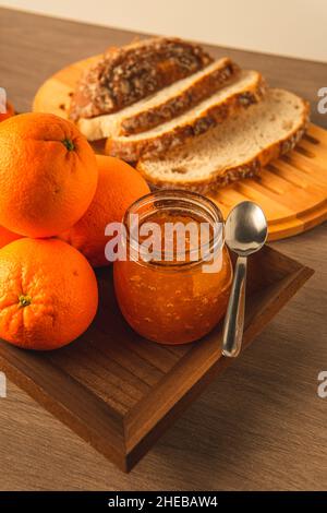 Sweet oranges, jam jar, bread and a spoon to spread and prepare a magnificent breakfast, on a rustic wooden tray Stock Photo