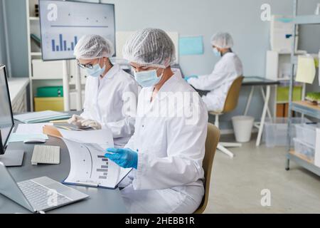 Group of scientists sitting at the table and working with statistics during pandemic in the laboratory Stock Photo
