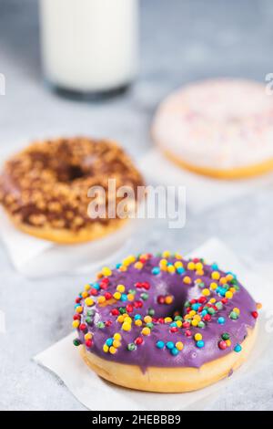Selection of donuts with different colors on a grey background with glass of milk Stock Photo