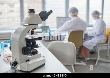 Close-up of microscope on the table in the laboratory with two scientists in the background Stock Photo