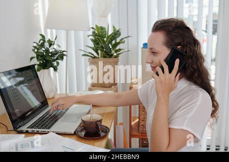 Smiling young project manager talking on phone with UI designer to discuss mobile application interface Stock Photo