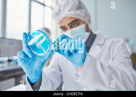 Young chemist in protective mask and gloves examining with blue liquid in tube in the laboratory Stock Photo