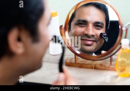 Handsome young Man using derma roller on face by looking at mirror - concept of treatment or therapy for skin, acne scarring and dermatology. Stock Photo