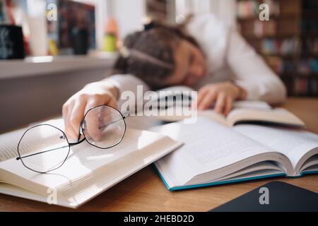 Young women got asleep on the books while studying holding reading glasses Stock Photo