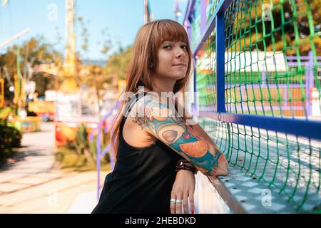 Portrait of a tanned young woman with tattoos posing near a fence. The concept of freedom, loneliness and psychology. Stock Photo