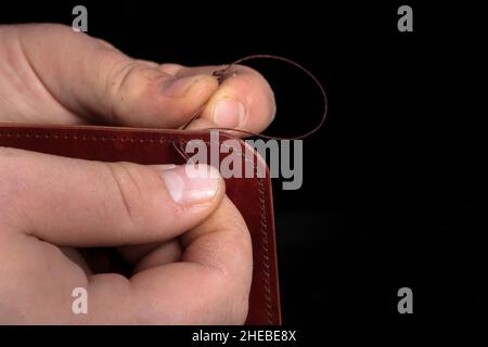 Making leather wallets. The hands of the master sew a leather product. Stock Photo