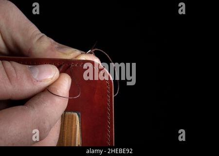 Making leather wallets. The hands of the master sew a leather product. Stock Photo