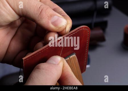 Making leather wallets. The hands of the master sew a leather product. Stock Photo