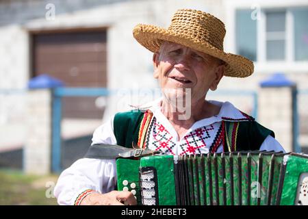 A Slavic Belarusian or Ukrainian man in a straw hat plays the accordion. Stock Photo