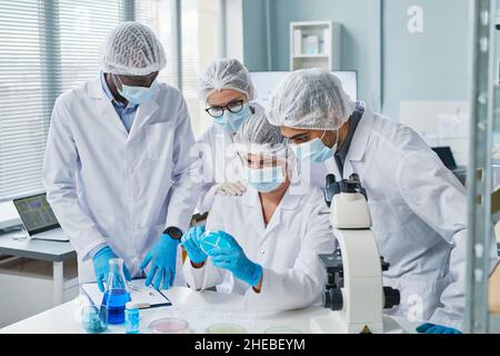 Group of scientists in protective masks examining samples in tube in team and developing new medicine from virus in the lab Stock Photo