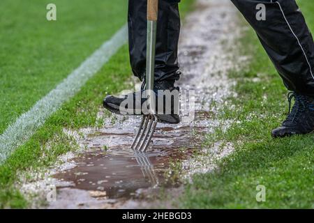 Member of ground staff aerating grass helping to drain water from waterlogged football pitch Stock Photo
