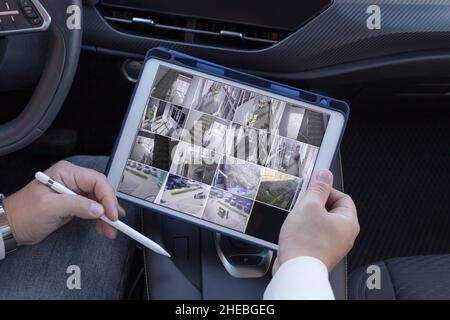 Man holding digital tablet with multiple camera views sitting in car Stock Photo