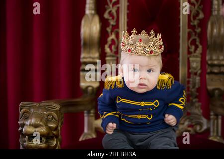 Funny kid for the royal crown on the royal throne. Stock Photo
