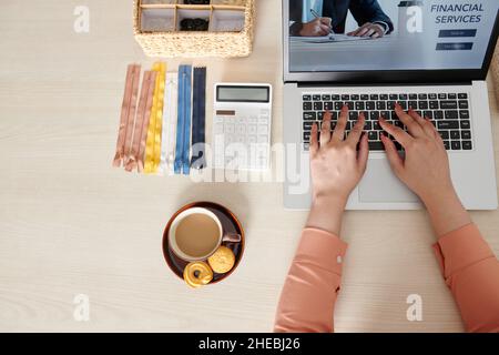 Hands of seamstess having cup of coffee with cookies and using website get financial services Stock Photo