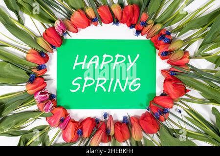 Beautiful flower frame of red tulips with the text Happy Spring on a green background. Stock Photo