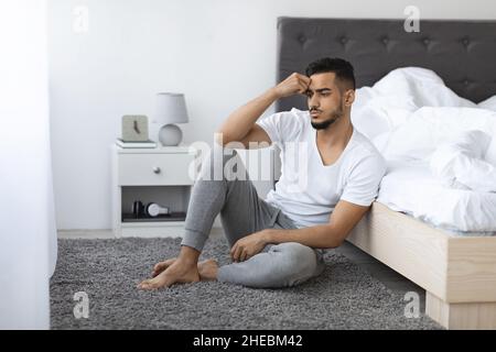 Melancholy Concept. Thoughtful Upset Arab Man Sitting On Floor In Bedroom Stock Photo