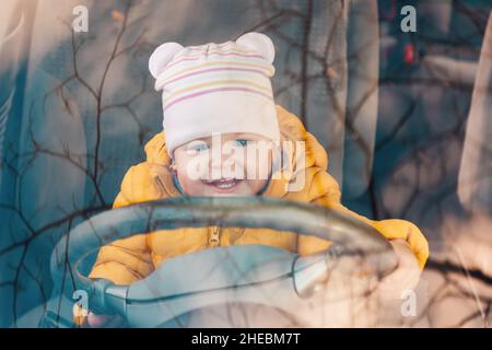 A little joyful child is sitting at the wheel of a car. View through the windshield of the auto. Driving training concept. Stock Photo