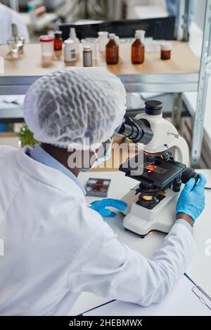 African scientist sitting at his workplace and working with microscope ...