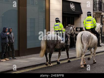 Two mounted policemen on police horses in central London watched by two young men Stock Photo