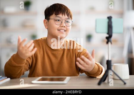 Cheerful asian teenager vlogger streaming from home, using cellphone Stock Photo