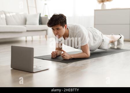Sporty asian man doing plank watching tutorial on laptop Stock Photo